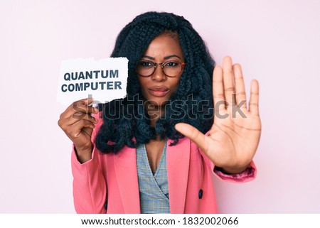Beautiful african woman holding quantum computer banner with open hand doing stop sign with serious and confident expression, defense gesture 