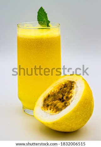 Passion fruit juice. Glass of passion fruit juice with mint leaf on the edge of the glass and half a passion fruit cut next to the glass, isolated on white background. Royalty-Free Stock Photo #1832006515