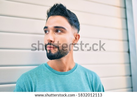Young arab man with relaxed expression leaning on the wall at the city.