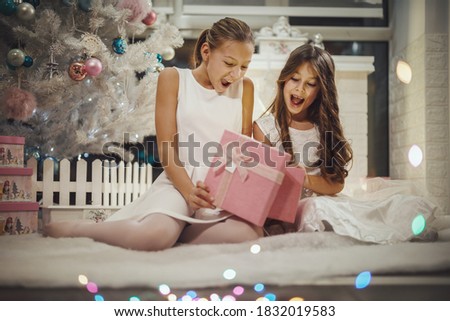 Shot of a two excited little girls opening their Christmas gifts by a white Christmas tree at the home.