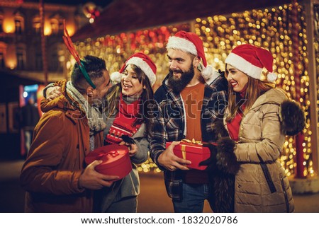 Shot of a group of cheerful young friends with Xmas gifts having fun at a night out.