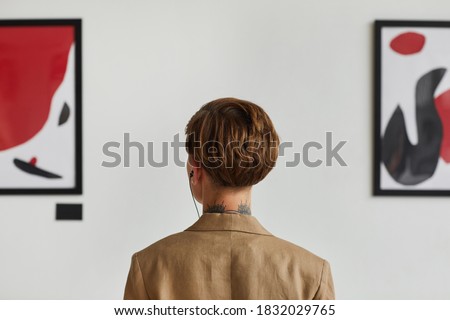 Graphic back view portrait of tattooed young woman looking at paintings and listening to audio guide at modern art gallery exhibition, copy space Royalty-Free Stock Photo #1832029765