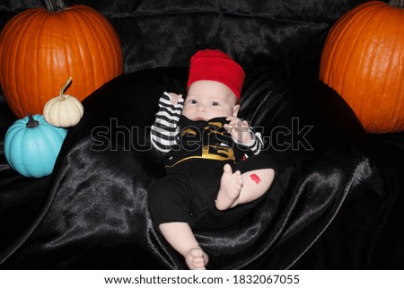 Baby dressed in pirate outfit by pumpkins