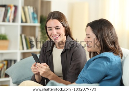 Happy friends sitting on a couch at home checking smart phone content