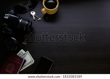 Top view of dark wooden desk with reflex digital camera, an smartphone, passport, keys, coffee cup and money. Copy space.