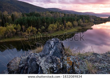 Autumn landscape. River at sunset under a dramatic sky. Rocks in the foreground and mountains in the background. Beauty of nature. Change of seasons of the year. 