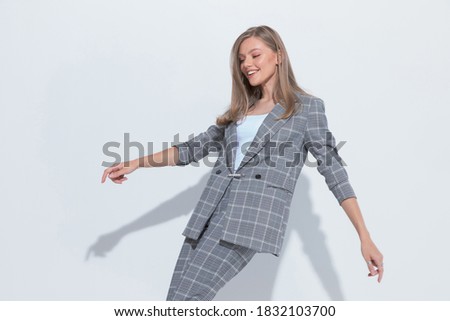 Cheerful fashion businesswoman laughing, wearing suit while dancing on white studio background