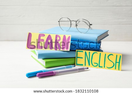 Phrase LEARN ENGLISH, books, glasses and felt tip pens on white wooden table