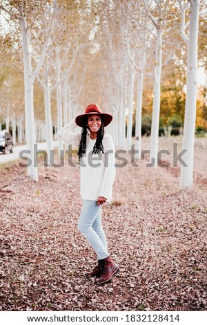 portrait of mid adult hispanic woman wearing a hat at sunset during golden hour, autumn season, beautiful path of trees background