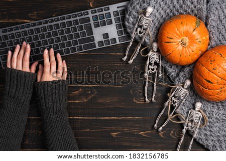 Female hands and Halloween decorations with skeleton and laptop