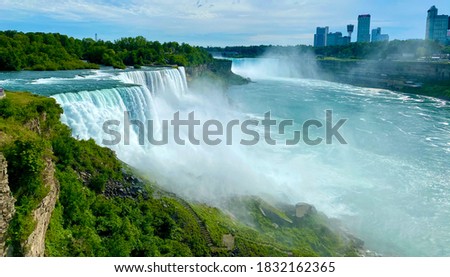 View of the American Falls seen from Niagara Falls, NY. The skyline of Niagara Falls, Ontario Canada sits in the background.