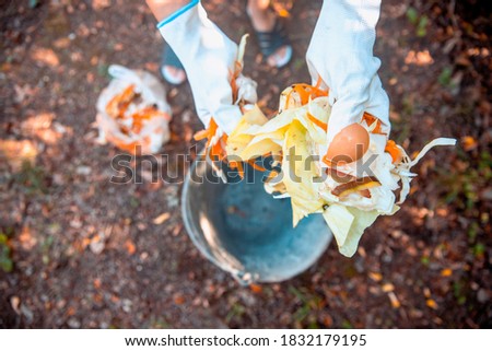 Female hands in gloves throwing Biodegradable Food remains in the Bucket bin. Composting organic food waste. Good for manuring of a Garden