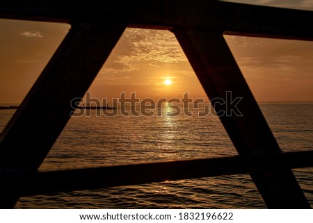Sun rising between the railings of the walkway,sea, orange, picture