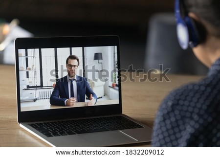 Back close up view of employee in headphones have video call with employer on laptop in office. Worker in earphones talk on webcam digital virtual conference, engaged in online meeting on computer. Royalty-Free Stock Photo #1832209012