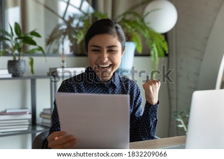 Overjoyed young indian female employee read good news in post paper letter at workplace. Happy millennial mixed race ethnicity woman get unexpected pleasant message in postal letter correspondence. Royalty-Free Stock Photo #1832209066