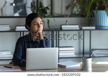 Thoughtful young indian businesswoman sit at desk distracted from computer work look in distance thinking. Pensive ethnic female employee make plan or decision in office. Business vision concept. Royalty-Free Stock Photo #1832209102