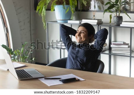 Happy indian woman worker sit relax in chair in office relieve negative emotions after working day. Smiling calm ethnic female employee rest at workplace dreaming or thinking. Stress free concept. Royalty-Free Stock Photo #1832209147