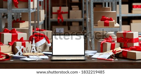 Laptop computer with white blank empty mock up screen on Merry Christmas table with presents gifts boxes in warehouse background. Ecommerce website xmas online shopping and shipping delivery, banner. Royalty-Free Stock Photo #1832219485