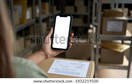 Female warehouse worker seller, small stock business owner holding phone mock up screen ad scan retail package parcel bar code on commercial shipping box delivery order on smartphone using mobile app.