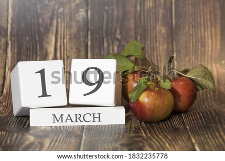 March 19. Day 19 of month. Calendar cube on wooden background with red apples, concept of business and an important event. Spring season.