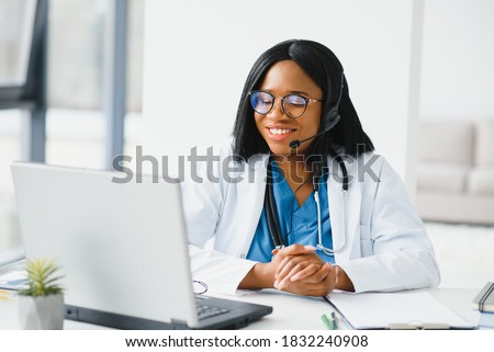 African doctor wear headset consult patient make online webcam video call on laptop screen. Telemedicine videoconference remote computer app virtual meeting. Over shoulder videocall view. Royalty-Free Stock Photo #1832240908