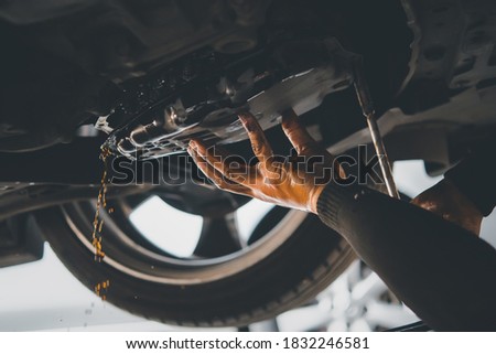 Car mechanic drain the old automatic transmission fluid (ATF) or gear oil at car garage for changing the oil in a gear box of car engine Royalty-Free Stock Photo #1832246581