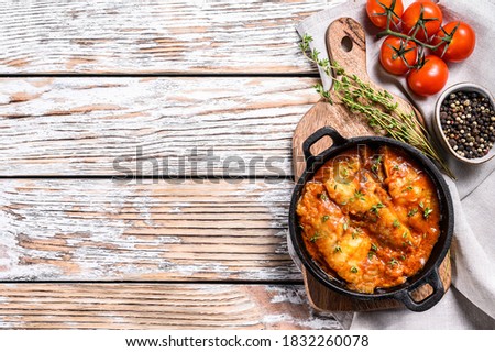 tilapia fish baked in tomatoes in a pan. White wooden background. Top view. Copy space