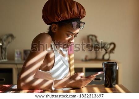 african american woman wearing showercap looking at smartphone during morning routine Royalty-Free Stock Photo #1832313697