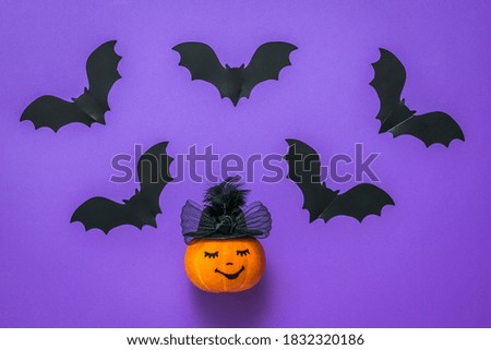Black silhouettes of bats and a pumpkin in a hat on a purple background. The concept of the Halloween celebration.