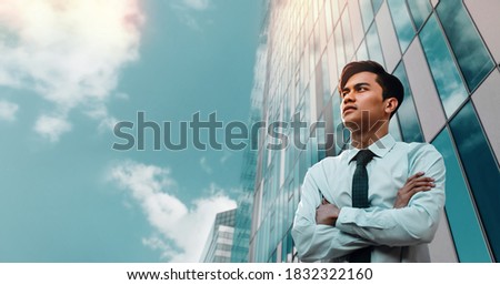 Portrait of a Striving Young Asian Businessman in the City. Crossed Arms and looking up into the Sky. Modern Office Building as background Royalty-Free Stock Photo #1832322160