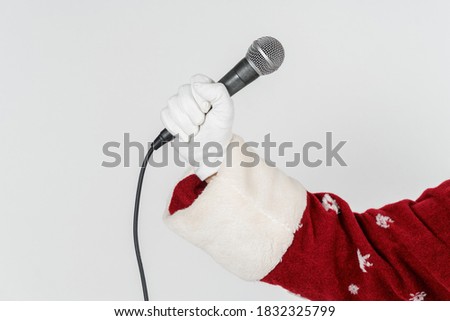 Holidays and Christmas concept. The hand of Santa Claus is holding a microphone in his hand. Isolated on white