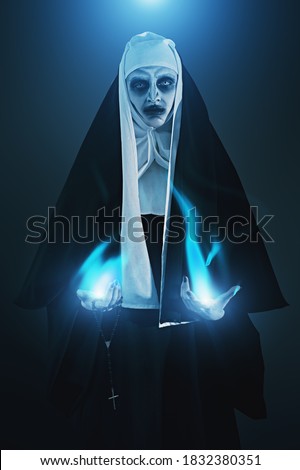 Evil cursed nun with a magical blue flame in her hands on a dark background. Halloween and Horrors. 