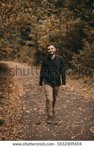 Portrait of a young handsome European man in a green shirt and beige pants walks in the autumn yellow park. Lonely, dreamer, in search of himself, progress, style.
