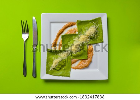 Green ravioli with spinach and meat inside and parmesan cheese on top served in white square plate over bright green background. Delicious Italian cuisine concept. Green screen.