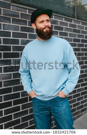 City portrait of handsome hipster guy with beard wearing blue blank sweatshirt with space for your logo or design. Mockup for print