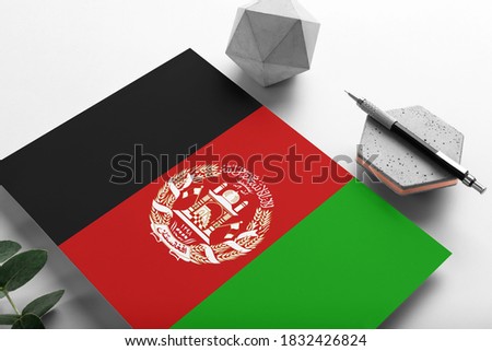 Afghanistan flag on minimalist paper background. National invitation letter with stylish pen on stone. Communication concept.