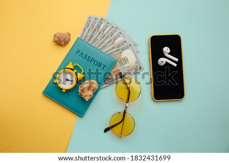 Summer vacation composition. Sunglasses, smartphone, shell and passport with money banknotes on blue yellow background