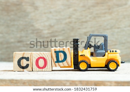 Toy forklift hold letter block D to complete word COD (abbreviation of cash on delivery) on wood background
