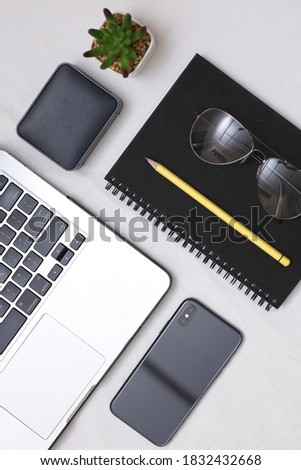 Top view of open laptop ready to work standing on the white table above. speaker smart phone sunglasses and black notebook with a pencil