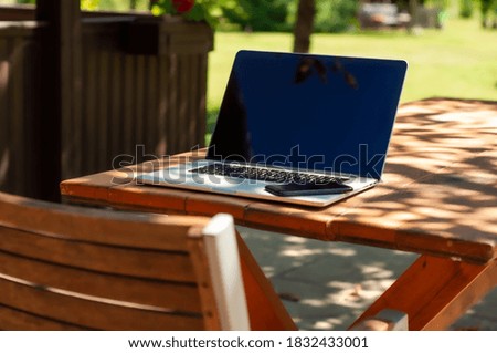 View on a laptop pc and a smartphone and acoffee mug on a table in the garden in a home office or home school enviroment on a sunny day.