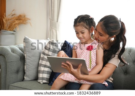 Mother and daughter watching tv on tablet on couch in living room.