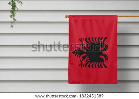 Albania national small flag hangs from a picket fence along the wooden wall in a rural town. Independence day concept.