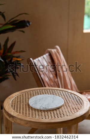 Stylish living corner setting with circular marble tray on rattan wood table and artificial plant in basket in the background / cozy interior design / copy space Royalty-Free Stock Photo #1832462314