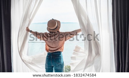 Rear back view woman opening white curtains enjoy sea view, Happy  traveller stay in high quality hotel. Royalty-Free Stock Photo #1832474584