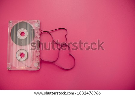 An old vintage cassette tape with the tape being pulled out in the shape of two love hearts on a pink and red background mixed tape music poster concept