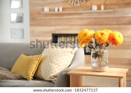 Beautiful flowers in vase on table in room, closeup. Cozy interior inspired by autumn colors