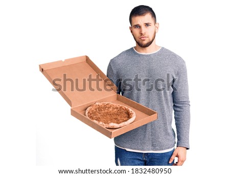 Young handsome man holding delivery italian pizza thinking attitude and sober expression looking self confident 