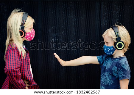 Funny little children in headphones listening music keep social distance on outside street walk. Kids wearing protective face masks for outside walk due coronavirus Covid-19 disease pandemic.