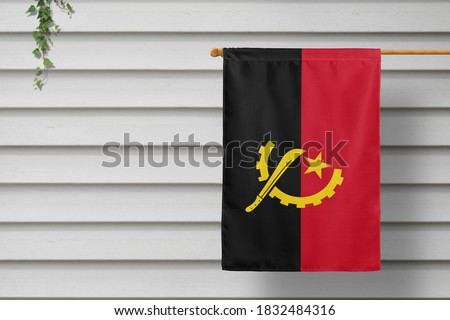 Angola national small flag hangs from a picket fence along the wooden wall in a rural town. Independence day concept.