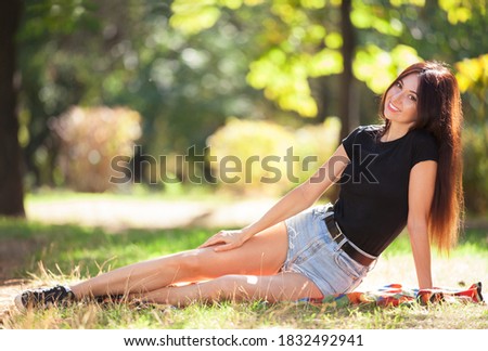 Young woman relax in the park on green grass. Beauty nature scene with colorful background, trees at summer season. Outdoor lifestyle. Happy smiling woman sitting on green grass